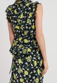 Svart klänning med blommigt och citronmönster, som har en volangmidja och genomskinliga, spetsiga ärmar som tillför textur och detalj.