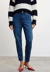 Jean en denim bleu moyen avec une coupe slim et une taille haute, associé à un pull rayé noir et blanc et des talons pointus rouges.