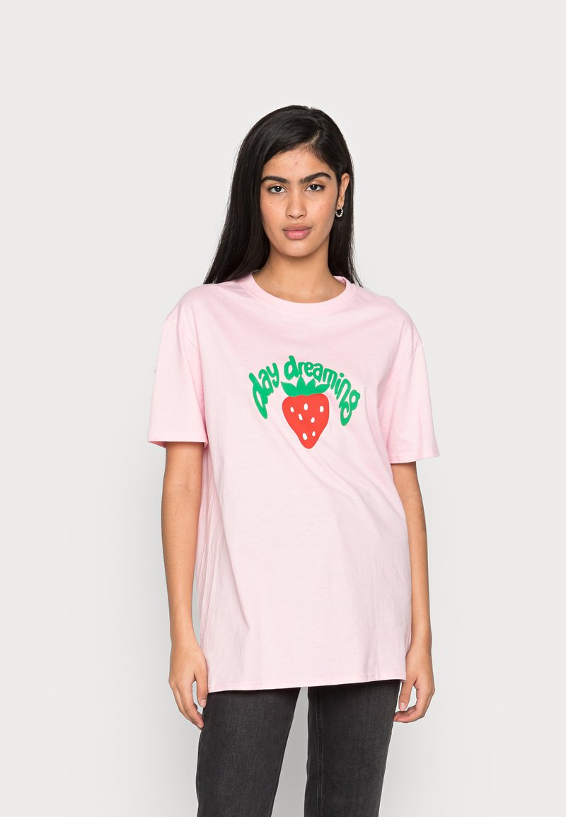 T-shirt de algodão rosa claro com texto verde "day dreaming" e um gráfico de morango vermelho com pontos brancos. Corte descontraído e mangas curtas.