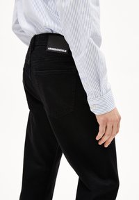 Jeans en denim noir à coupe droite, dotés d'une étiquette au dos portant la mention "ARMEDANGELS" et de subtils détails de couture sur les poches.