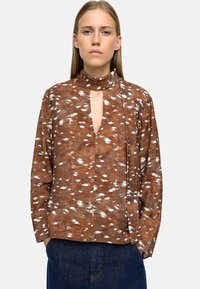 Brązowa, wzorzysta koszula z długim rękawem i kołnierzykiem, z głębokim dekoltem w kształcie litery V oraz białymi akcentami w postaci pociągnięć pędzla; wykonana z miękkiego, lekkiego materiału.