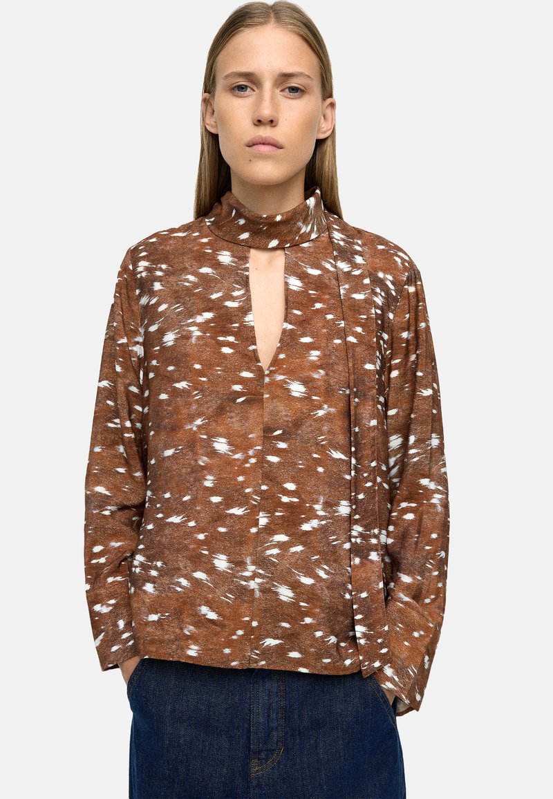 Brązowa, wzorzysta koszula z długim rękawem i kołnierzykiem, z głębokim dekoltem w kształcie litery V oraz białymi akcentami w postaci pociągnięć pędzla; wykonana z miękkiego, lekkiego materiału.
