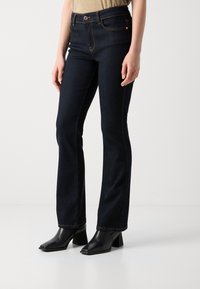 Mörkblå utsvängda jeans med hög midja, med orange sömmar, framfickor och bärs med svarta klackade ankelstövlar.