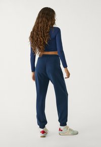 Marinefarbener langärmliger Crop-Top mit figurbetontem Design und marinefarbener Jogginghose mit elastischen Bündchen, kombiniert mit mehrfarbigen Sneakers.