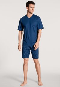 Marineblauwe V-hals t-shirt gecombineerd met gestreepte shorts in bijpassend marineblauw, met kleine lichtblauwe stippen. Katoenen stof, relaxte pasvorm.