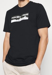 Black cotton t-shirt featuring a white graphic with "NIKE AIR" over clouds on the chest, short sleeves, and a crew neckline.