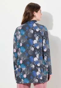 Langärmlige Tunika aus weichem Stoff, mit einem gemusterten Design von blauen, rosa und grauen Kreisen. Rüschen-Saum und runder Halsausschnitt.