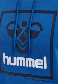 Hoodie bleu avec un logo noir prominent comprenant des formes abstraites, des cordons avec des accents bleus, et un slogan textuel en dessous du logo.