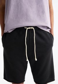 Shorts de sport noirs avec une taille élastique et un cordon blanc ; associés à un t-shirt lavande à manches courtes. Texture douce, design décontracté.