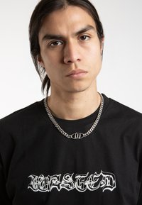 Un tricou negru cu litere gotice albe "WASTED" pe față. Un colier din lanț argintiu cu pandantiv oval. Textură de țesătură netedă.