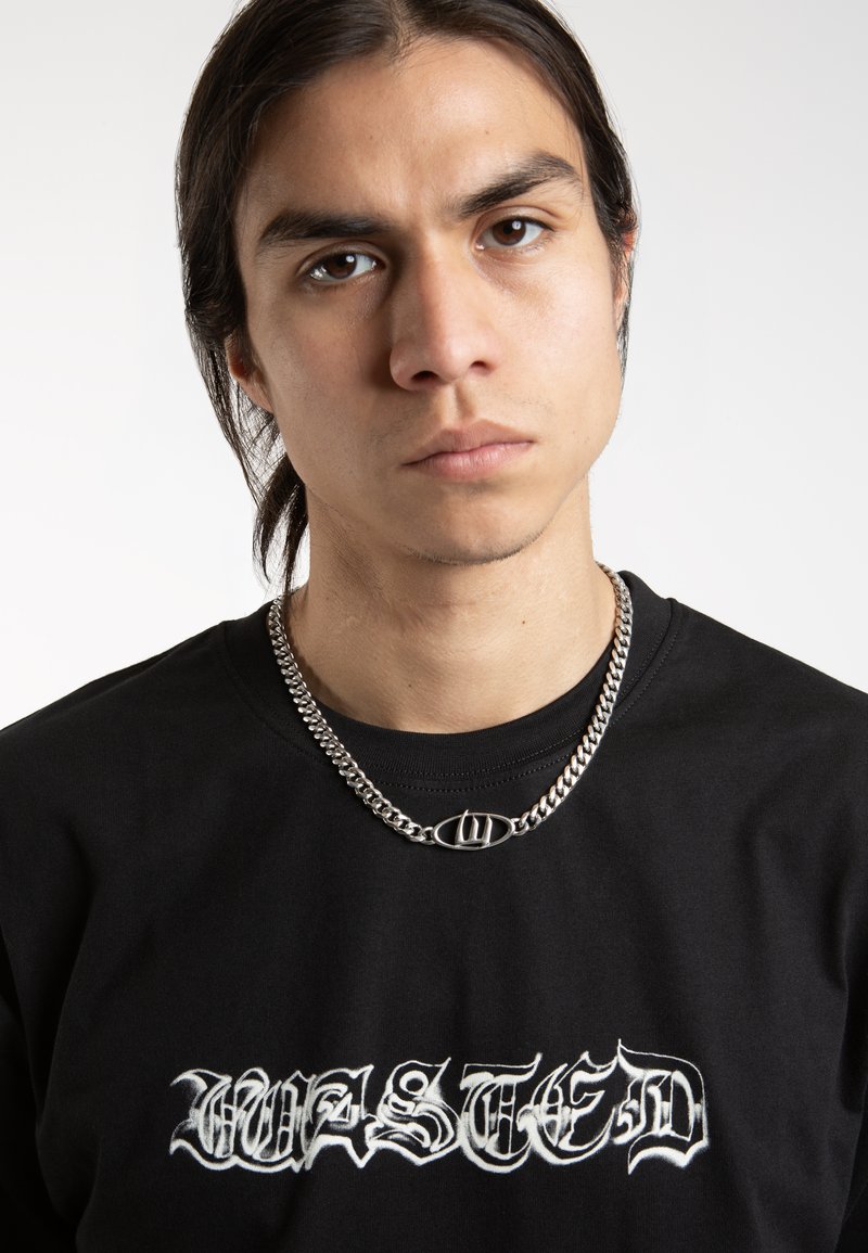 Un tricou negru cu litere gotice albe "WASTED" pe față. Un colier din lanț argintiu cu pandantiv oval. Textură de țesătură netedă.