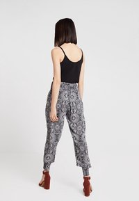 Schwarzes ärmelloses Top, kombiniert mit leichten, gemusterten Hosen in Schwarz und Weiß. Die Hosen haben einen elastischen Bund und schmal zulaufende Beine.