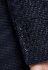 Navy tweedowy żakiet z mankietami z teksturowanej tkaniny, wyposażony w cztery czarne guziki i szczegółowe przeszycia na krawędzi.