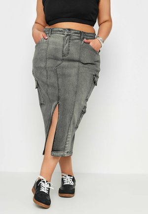 Falda de mezclilla gris con una abertura frontal, bolsillos laterales y una forma estructurada. Combinada con zapatillas negras con cordones blancos y una suela texturizada.
