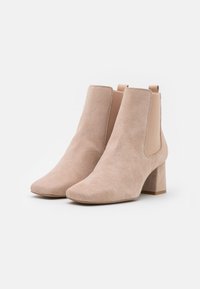 Botas de tobillo de ante beige con punta cuadrada, paneles laterales elásticos y un tacón grueso. Textura suave con un diseño minimalista; diseño versátil.