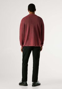 Gestrickter roter Pullover mit langen Ärmeln und rundem Ausschnitt, kombiniert mit schwarzen Hosen und schwarzen Schuhen, Rückansicht.