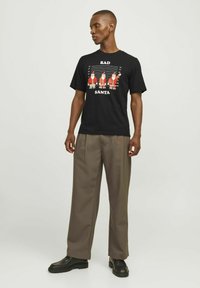Sort t-shirt med et grafisk motiv af julemandsskikkelser med teksten "BAD SANTA." T-shirten har en klassisk pasform og korte ærmer, lavet af bomuld.