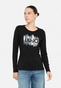 Must have pikkade varrukatega must särk ümmarguse kaelusega, millel on hõbedane ja must graafiline kujundus, mis kannab julgeid tähti "LUJO". Igapäevane lõige.