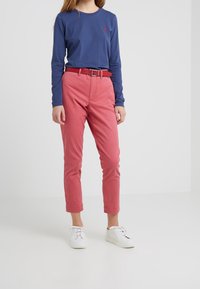 Tmavěmodrá košile s dlouhými rukávy a logem, spárovaná s růžovými kalhotami a bílými teniskami. Kalhoty mají přiléhavý střih a odpovídající opasek.