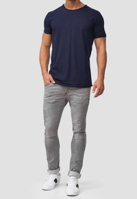 Navy short-sleeve t-shirt paired with slim-fit gray jeans, featuring a smooth texture and white athletic shoes with black accents.