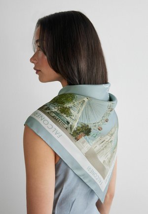 Kobieta o prostych ciemnych włosach nosząca jasnoniebieski szalik z ilustracjami diabelskiego młyna i budynków.