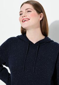 Námořnická modrá mikina s texturovaným pletením a žíhaným vzorem, se stahovací kapucí a volnějším střihem. Dlouhé rukávy, casual design.
