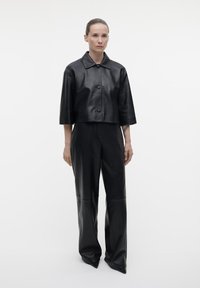 Zwarte leren cropped jack met een kraag en knopen aan de voorkant, gecombineerd met hooggewaisted wijde leren broek. Soepele textuur, minimalistisch ontwerp.