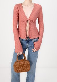 Rostfärgad ribbad stickad topp med djup V-ringning och knytdetalj, i kombination med högmidjade ljusblå jeans och en liten brun vadderad handväska.