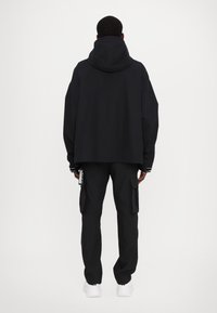 Black hooded jacket with a loose fit, paired with black cargo pants featuring side pockets, complemented by white sneakers.