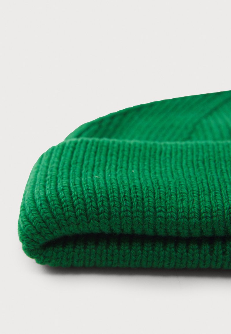 Groene gebreide muts gevouwen om de ribbelstructuur te tonen, met dikke garen. Het ontwerp heeft een gladde, zachte afwerking met een levendige kleur.