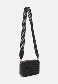 Bolso cruzado negro con textura trenzada en la parte frontal, herrajes dorados y una correa perforada. Forma rectangular, diseño elegante.