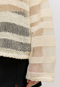 Leichtes Strickpullover in Creme mit horizontalen Streifenmustern, verfügt über eine lockere Passform und weite Ärmel, die das strukturierte Design betonen.