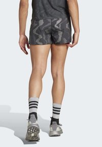 Schwarze Camo-Shorts mit strukturierter Oberfläche, kombiniert mit grau- und schwarzgestreiften Socken und leichten Sportschuhen mit Gummisohle.