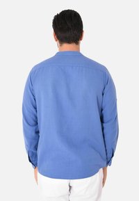Camicia azzurra a maniche lunghe realizzata in tessuto leggero, con polsini abbottonati e orlo arrotondato. La vista dal retro mostra una vestibilità rilassata e un design semplice.