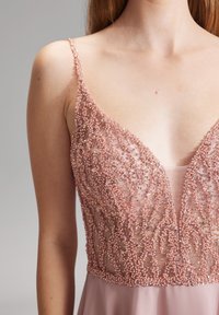 Różowa sukienka z koralikami o głębokim dekolcie w szpic i cienkich ramiączkach. Charakteryzuje się misternymi koralikami na przezroczystej warstwie i opadającą spódnicą.