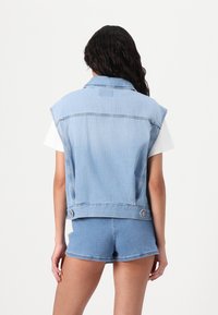 Light blue denim sleeveless jacket with a collar, two side buttons, and a smooth texture, worn over a white top and blue shorts.