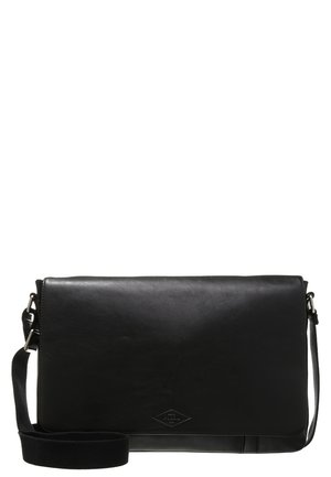 Sac à épaule en cuir noir avec fermeture à rabat et sangle réglable, forme rectangulaire, texture lisse et logo discret à l'avant.