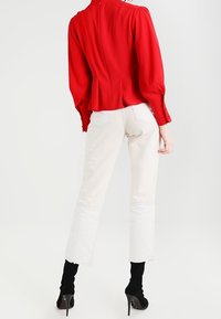 Rød bluse med pufsleeves, tekstureret stof og plisseret ryg, kombineret med cremefarvede vide jeans med rå kant, båret med sorte høje hæle.