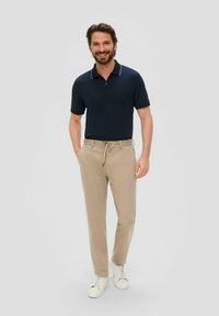 Granatowa koszulka polo z krótkim rękawem i zamkiem błyskawicznym, w zestawie z jasnobeżowymi spodniami z troczkami i białymi trampkami, na jasnoszarym tle.