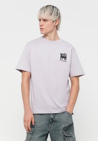 Lys lilla bomulds-T-shirt med korte ærmer, rund halsudskæring og et sort katte-grafik på venstre bryst. Bæres med grå cargo-bukser.