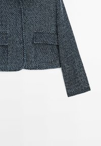 Blazer intrecciato in blu scuro con finitura strutturata, dotato di due tasche anteriori e maniche lunghe e dritte. Chiusure non visibili.