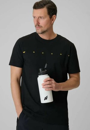 Man in een zwart "4F Sport" t-shirt houdt een witte waterfles met 4F-logo met open dop vast, kijkend naar links tegen een effen grijze achtergrond.