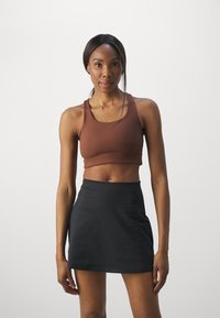Brun cropped tank top parret med en sort mini nederdel. Har en glat tekstur og enkelt design, med brede stropper og en tætsiddende silhuet.