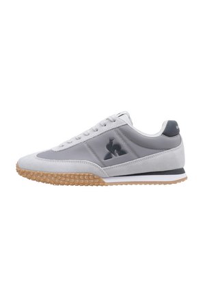 Chaussure de sport grise avec une tige en suède et en synthétique, présentant une semelle extérieure en caoutchouc, un bout arrondi et un détail de logo contrastant sur le côté.