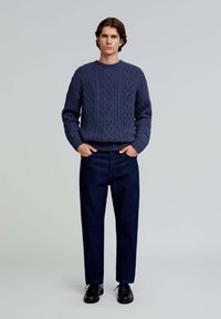 Navyblaue Kabelstrickjacke mit rundem Halsausschnitt, kombiniert mit dunkelblauen geraden Hosen und schwarzen Schuhen. Einfaches Design, texturierter Stoff.
