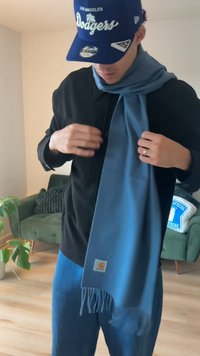 Lenço azul feito de tecido macio, com bordas frisadas e brilho sutil. Usado sobre uma camisa preta, com um boné azul e calças azuis.