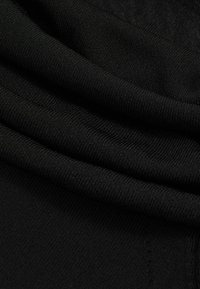 Tivă neagră cu un textură netedă, având pliuri suprapuse. Cusăturile sunt subtile, accentuând overall moliciunea și flexibilitatea.