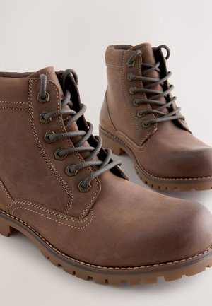 Bruine leren enkellaarsjes met grijze veters, een ronde neus en een robuuste rubberen zool. Voorzien van stikseldetails en zeshoekige veterogen.