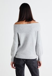 Light gray off-shoulder sweater with a ribbed neckline and long sleeves, made of soft material, paired with dark gray jeans.
