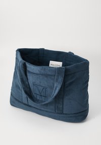 Navy blue tote bag made of plush fabric, featuring two sturdy handles and an embossed logo. Spacious interior with a soft texture.